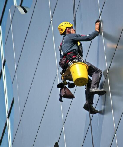 High rise window cleaner on ropes hangs from the side of a building and washes the exterior.