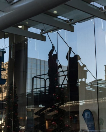 Commercial window cleaners wash the outside of a tall glass building downtown.