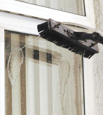 A specialized window cleaning tool with water jets and a brush is used to reach and wash tall windows.