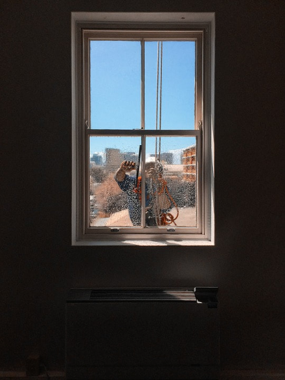 Photo of a view from the inside of an apartment as a window washer cleans the outside glass with a squeegee.