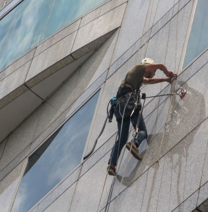 Skyscraper window cleaner hangs from ropes and clears dirt off the side of the building.